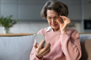 Attractive senior woman squints at her phone, frustrated with the cloudy vision caused by her cataracts.