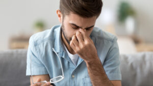 Man with dry eyes removes his glasses and rubs his eyes